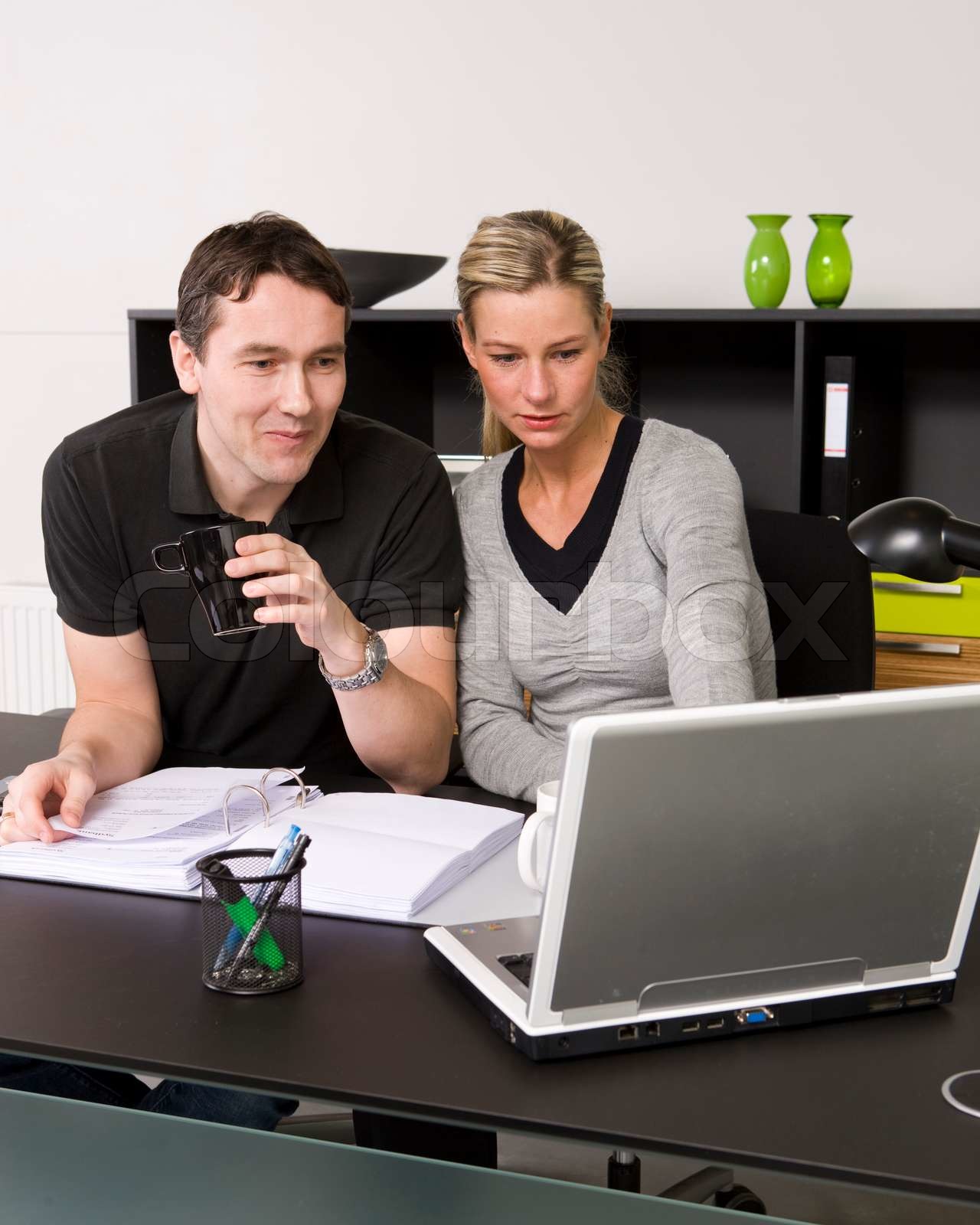 A male and female office workers looking at the screen of their laptop ...
