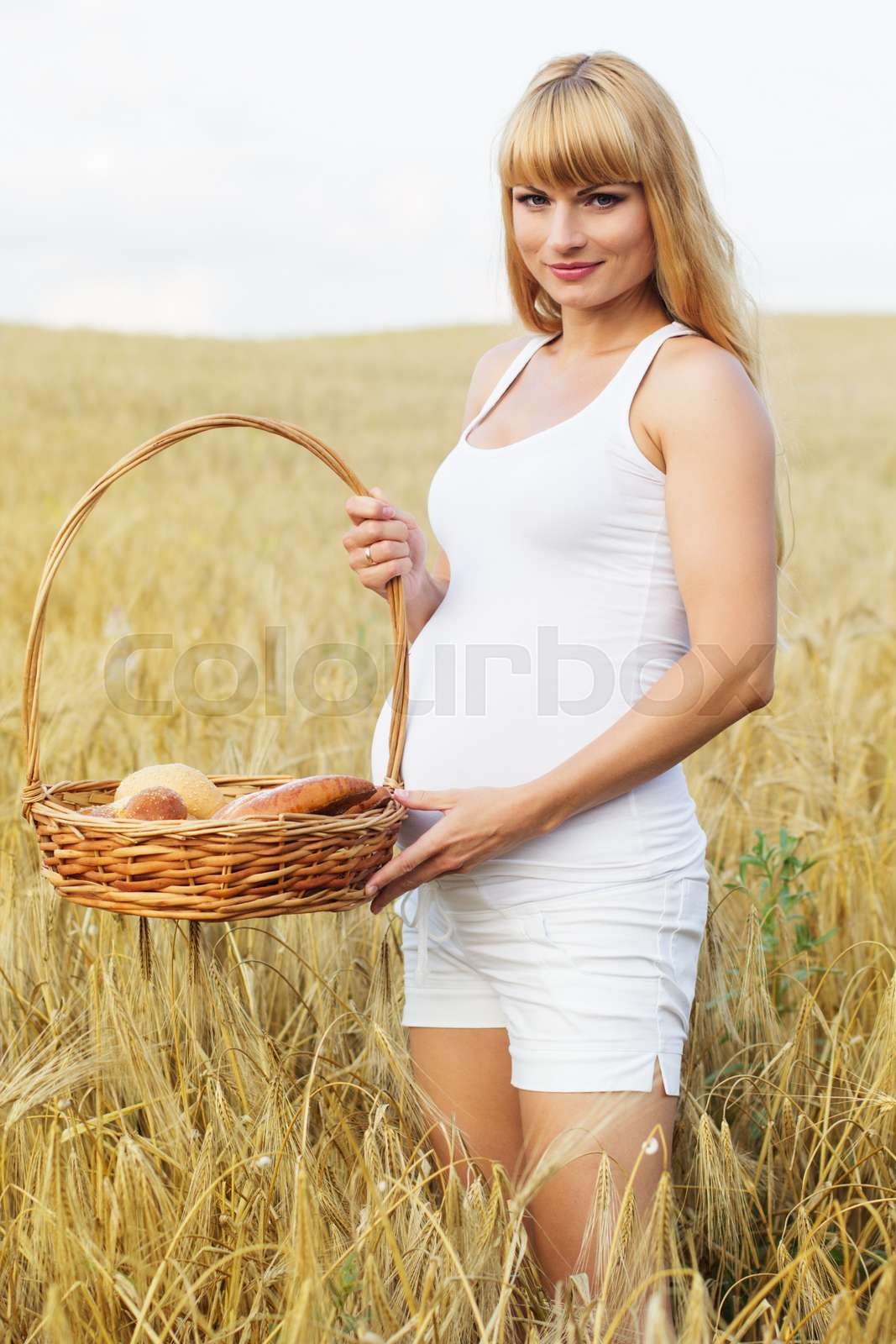 Pregnant girl in wheat field with basket of fresh buns Stock image