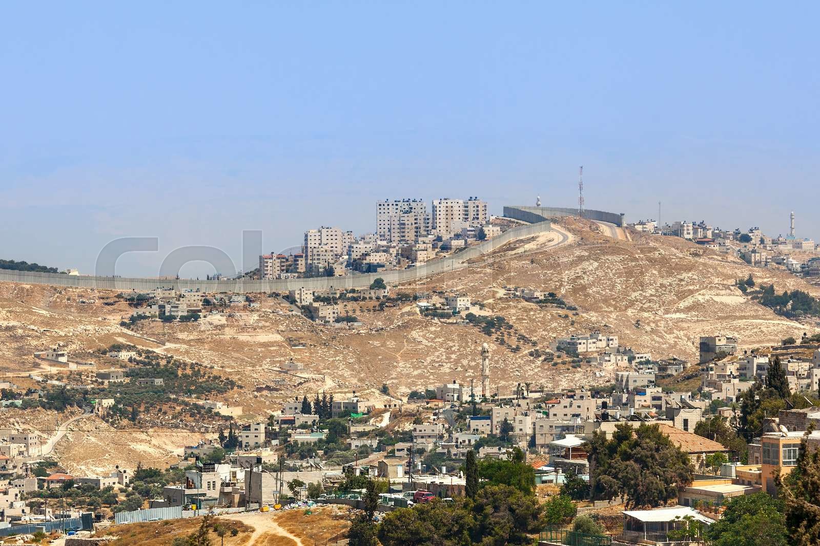 Palestinian village and town on the hill behind separation wall on the