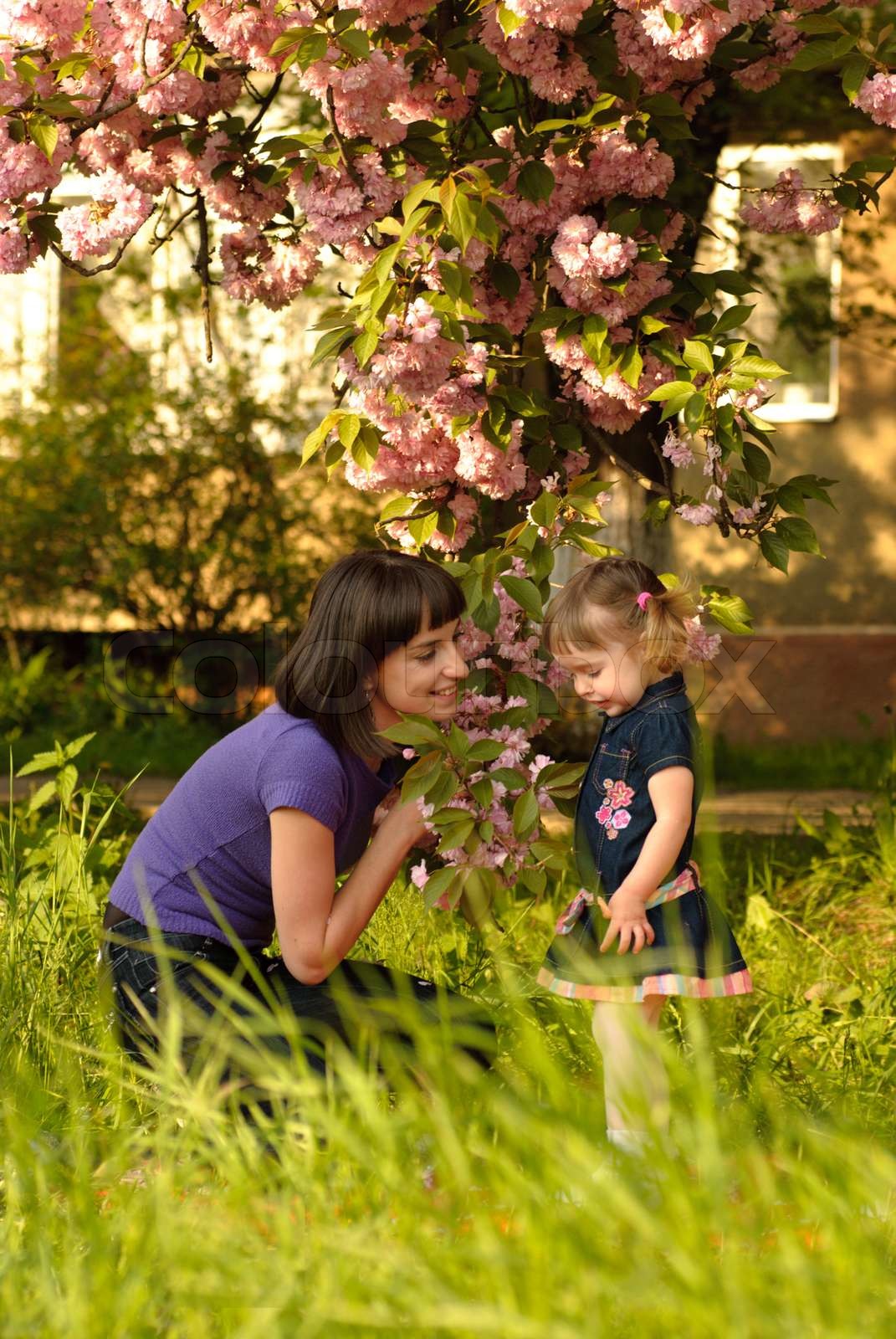 Kleines Mädchen im Garten mit Mutter, unter dem sakura Baum. Stock