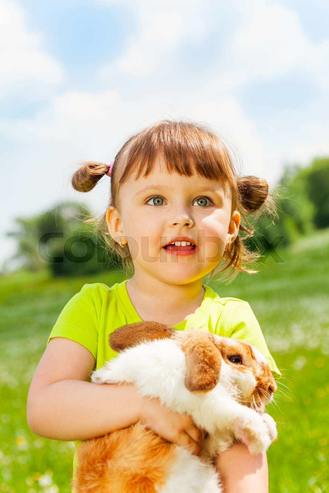 Looking small girl hugging rabbit in green field | Stock image | Colourbox