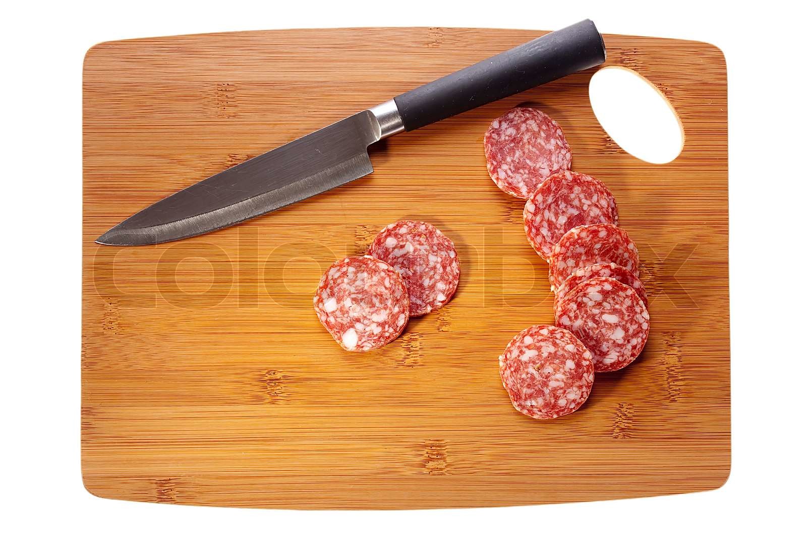 Sliced salami laying next to a knife on a brown cutting board. Stock image Colourbox