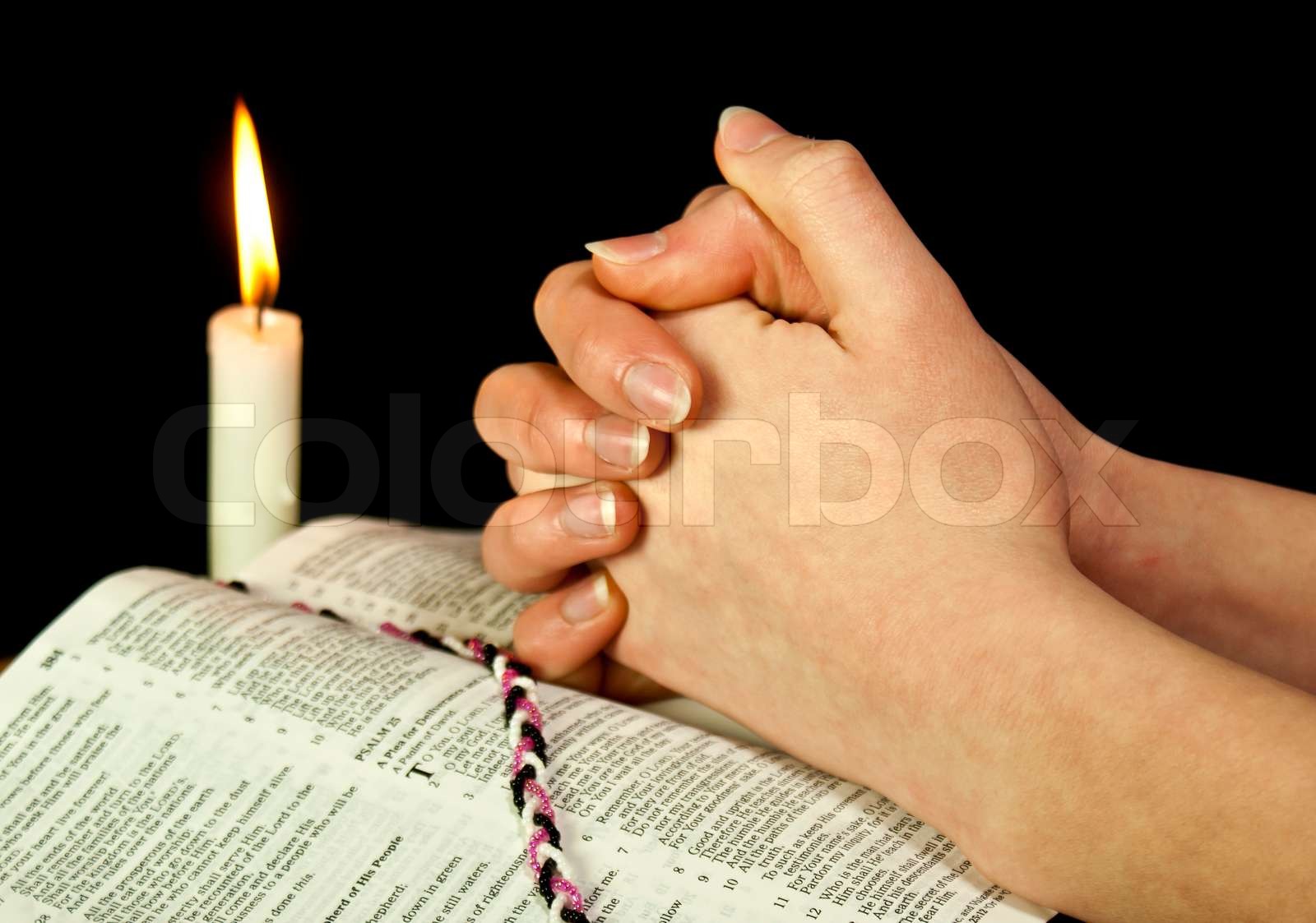 Open Bible with burning candle and hands of praying woman Stock image
