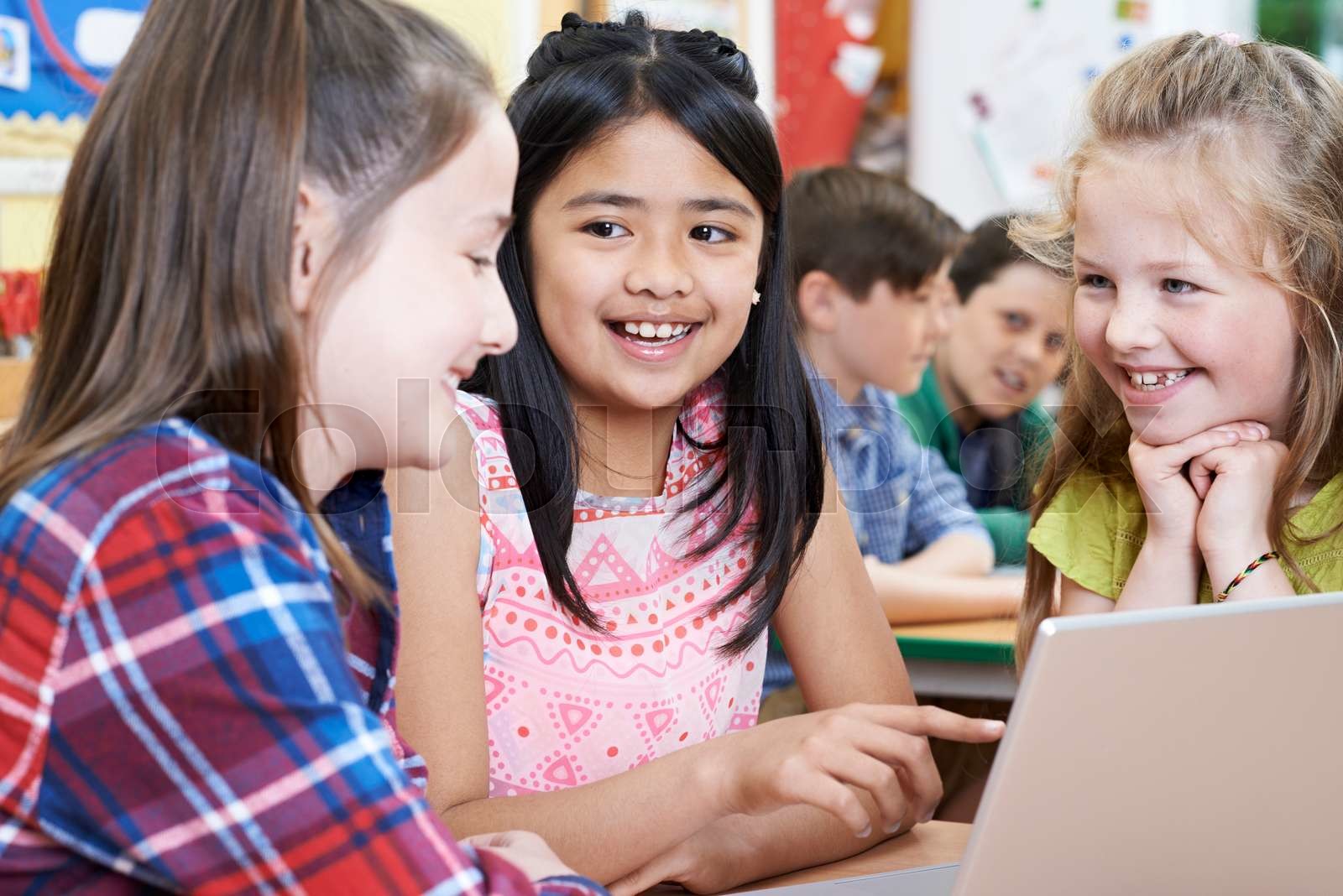 Group Of Elementary School Children Working Together In Computer Class 