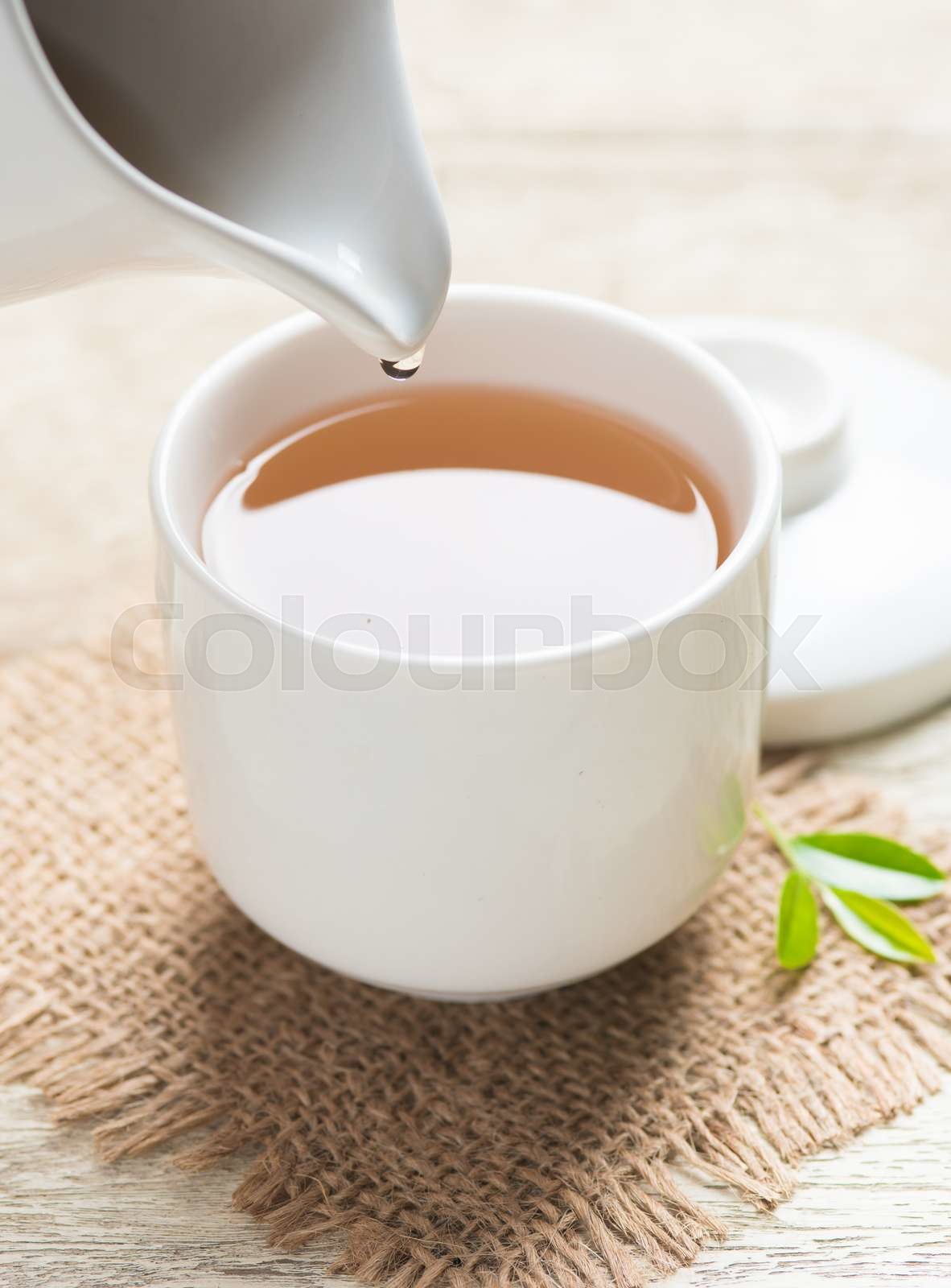 Pouring tea from jug to cup of tea and tea leaves on wooden Stock