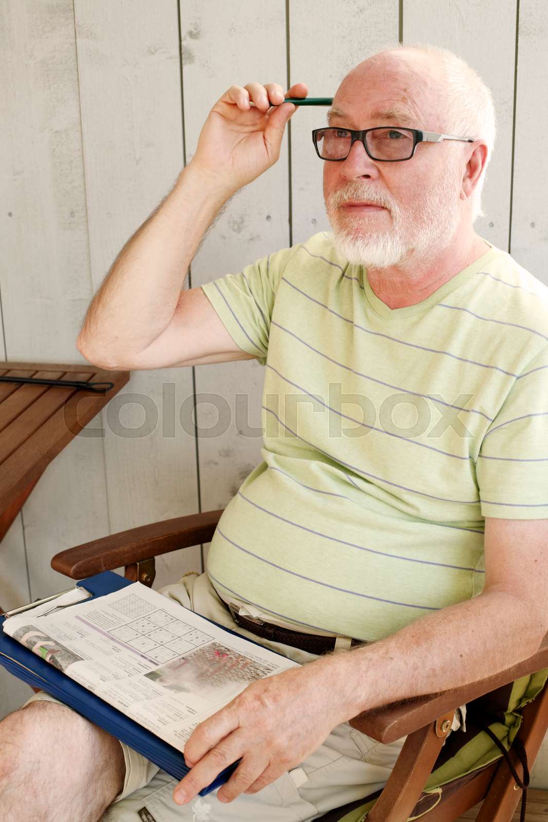 Senior Man Sitting On Terrace In Summer Solving Sudoku Puzzle 