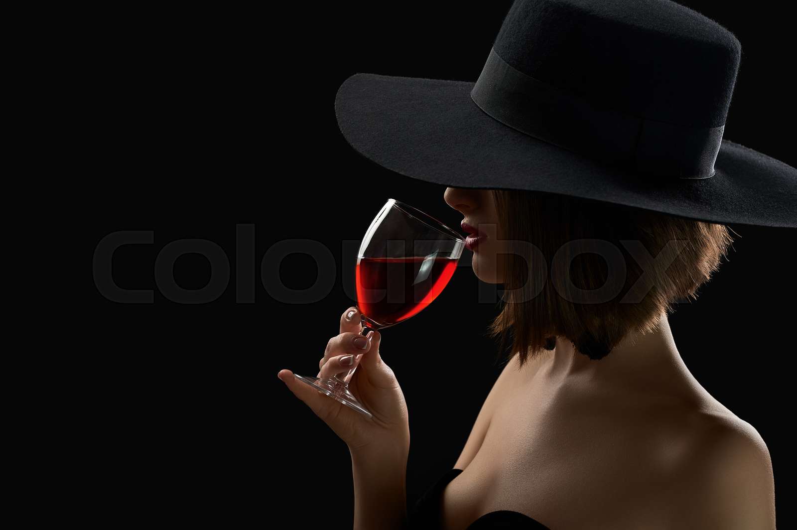 Elegant mysterious woman in a hat holding a glass of red wine on ...