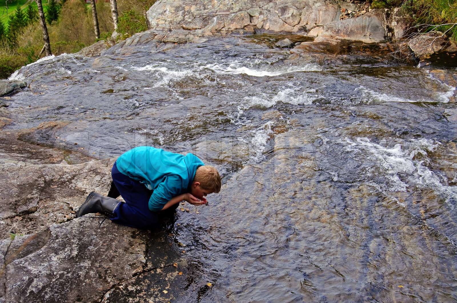 A young boy drinking water from the river Stock image Colourbox