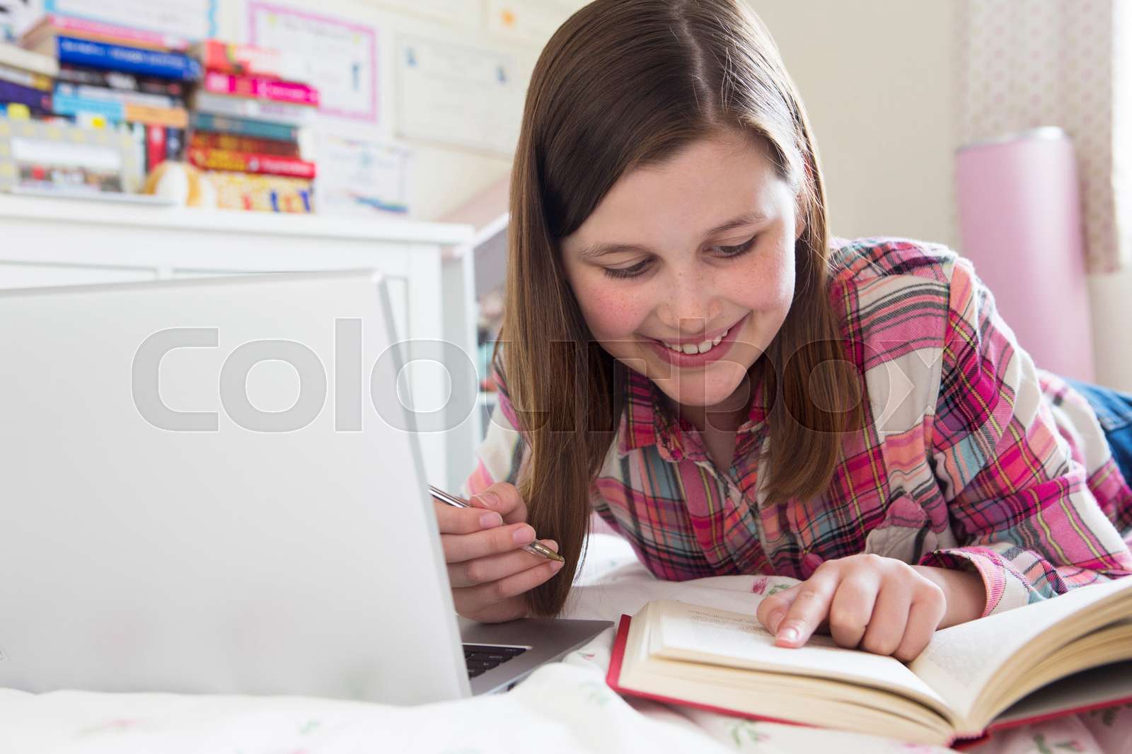 young-girl-lying-on-bed-doing-homework-using-laptop-stock-image