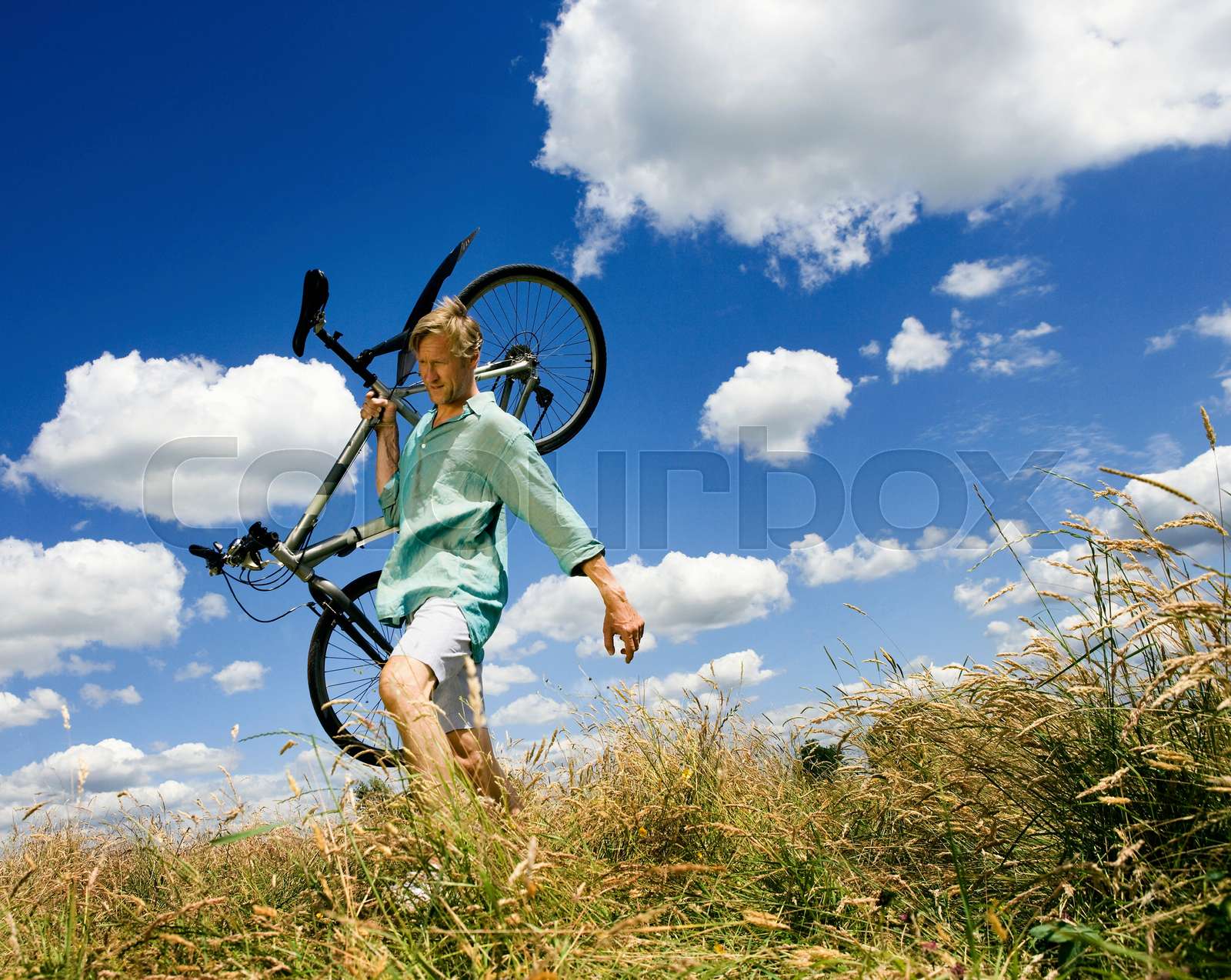 Man carrying cycle across field | Stock image | Colourbox
