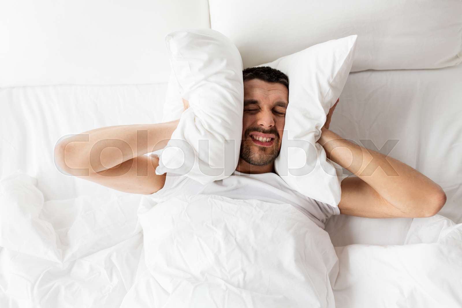 man in bed with pillow suffering from noise | Stock image | Colourbox