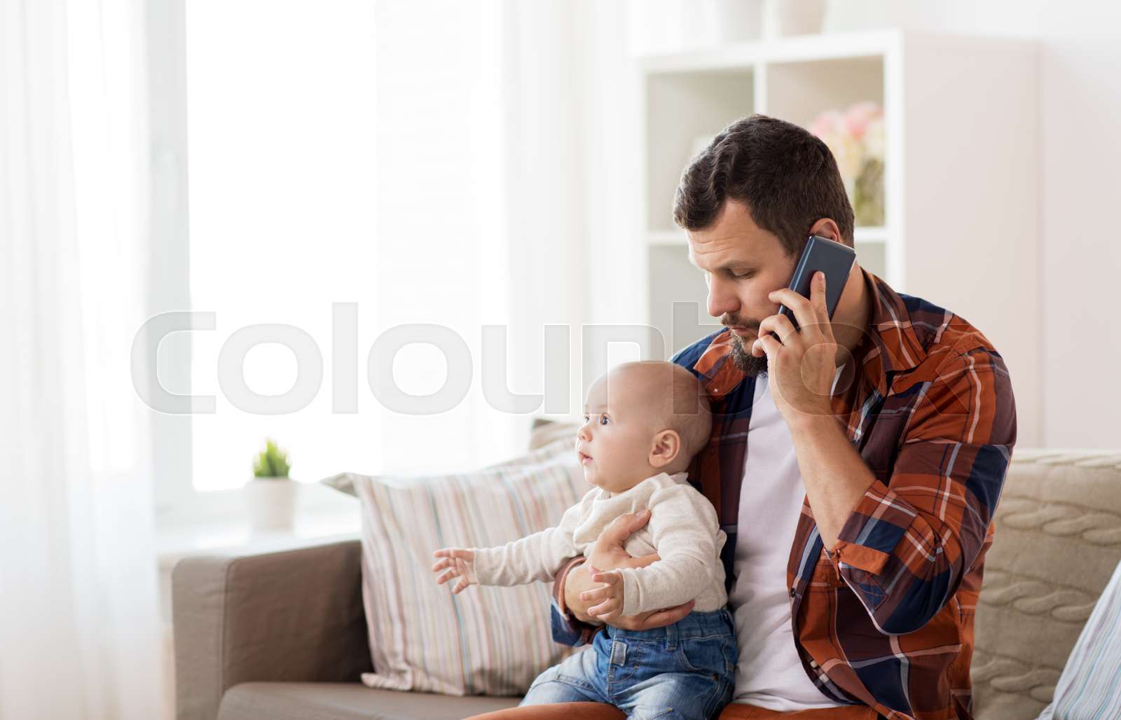 father with baby calling on smartphone at home Stock image Colourbox