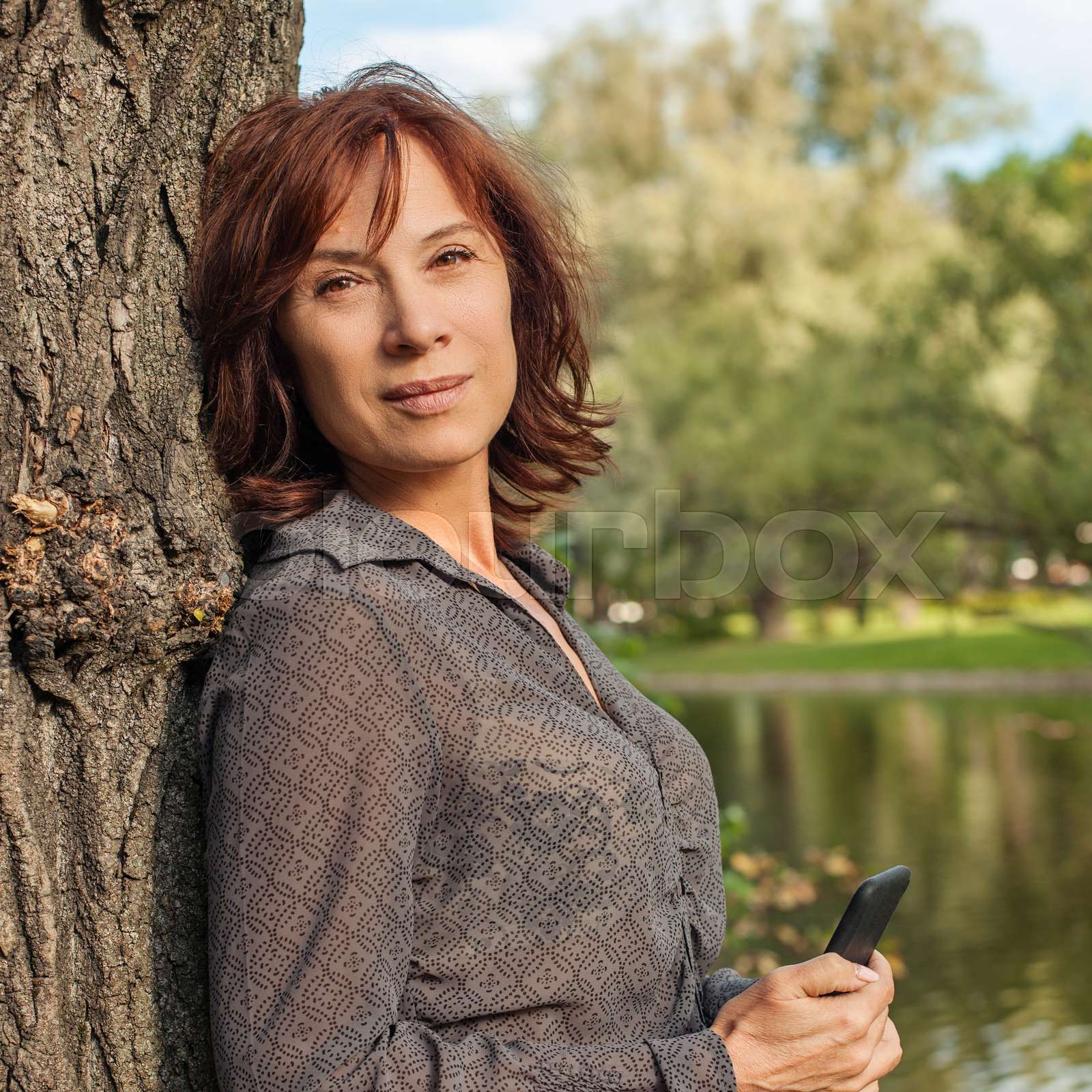 Mature woman outdoors portrait. Mid adult woman with smartphone