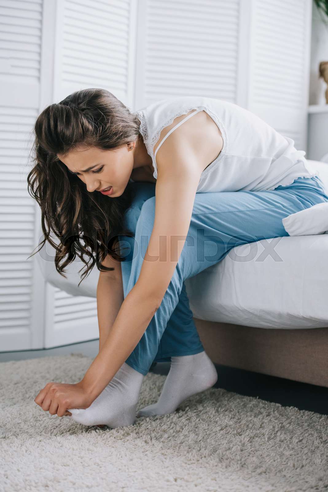 young woman suffering from foot pain while sitting on bed Stock image