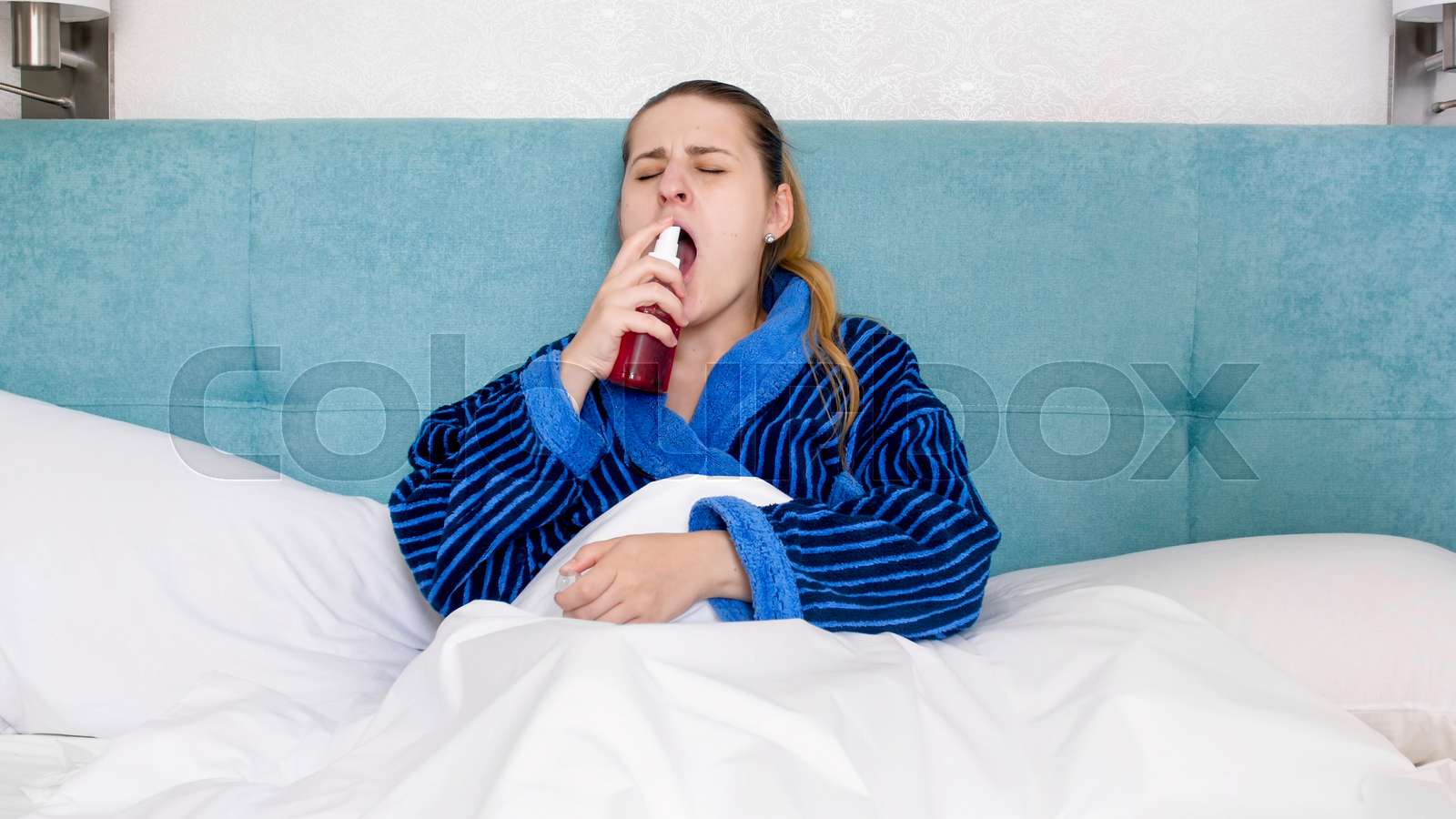 Portrait of sick woman with sore throat lying in bed and using throat