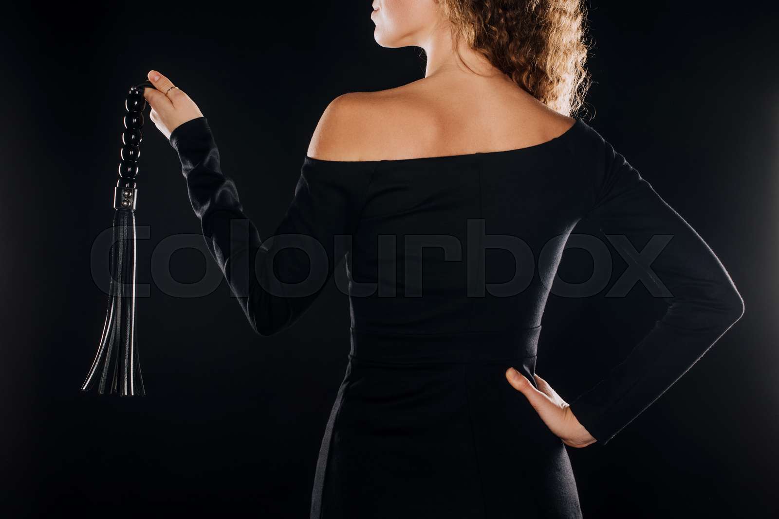 back view of curly woman holding leather flogging whip isolated on