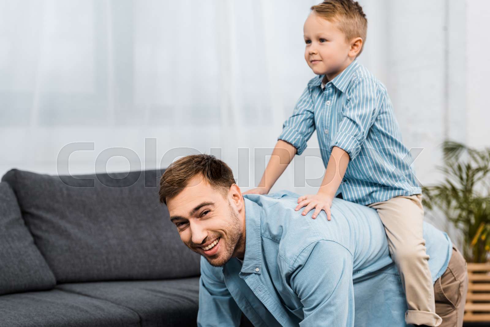 father standing on all fours and looking at camera while cute boy ...