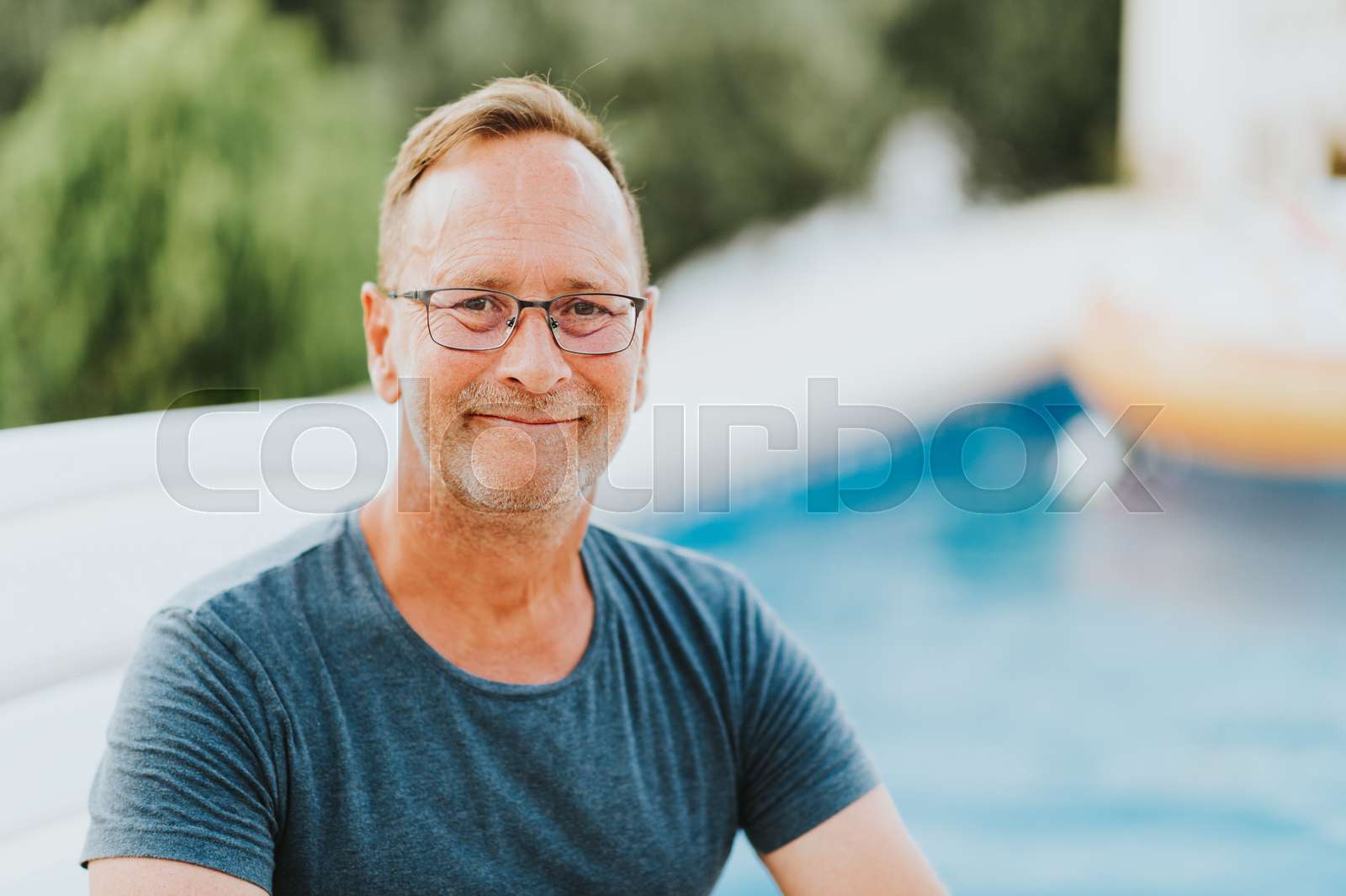 outdoor-portrait-of-50-year-old-man-resty-by-the-pool-wearing-blue-t