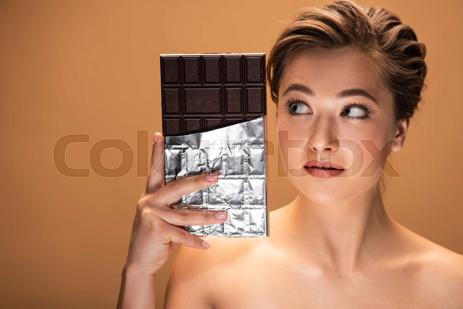beautiful young nude woman looking at chocolate bar in silver foil