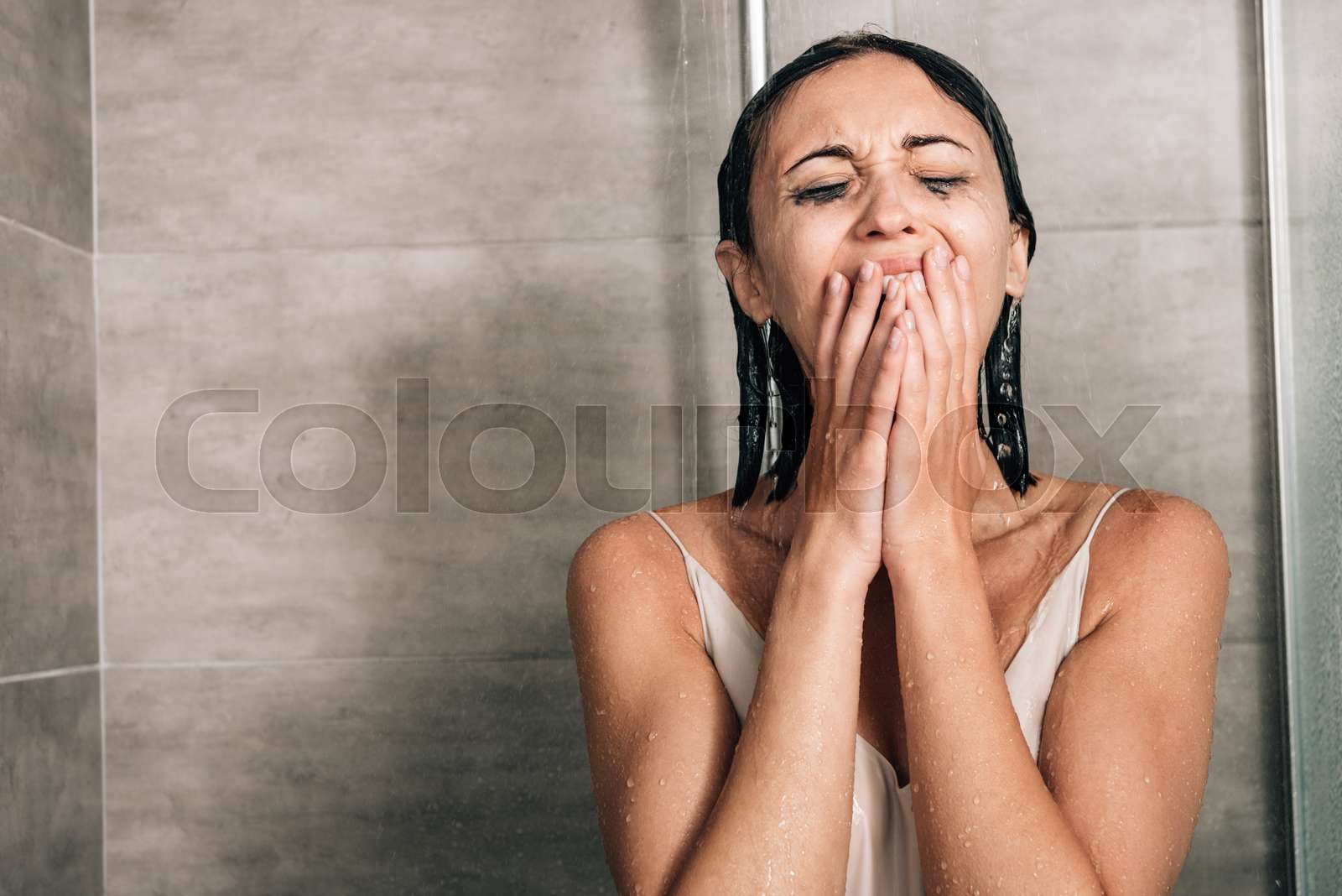 lonely depressed woman in shower covering mouth and crying at home