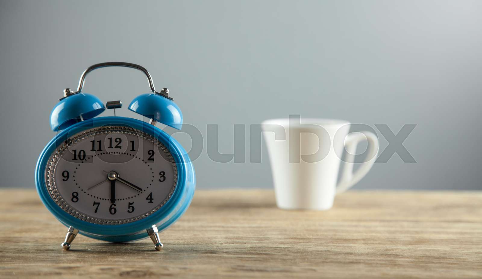 Alarm clock and white coffee cup on the wooden desk. Stock image