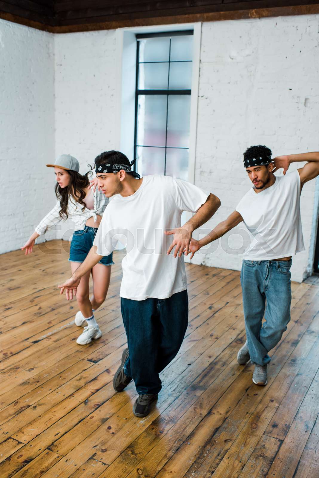handsome multicultural dancers in headbands and attractive girl in cap