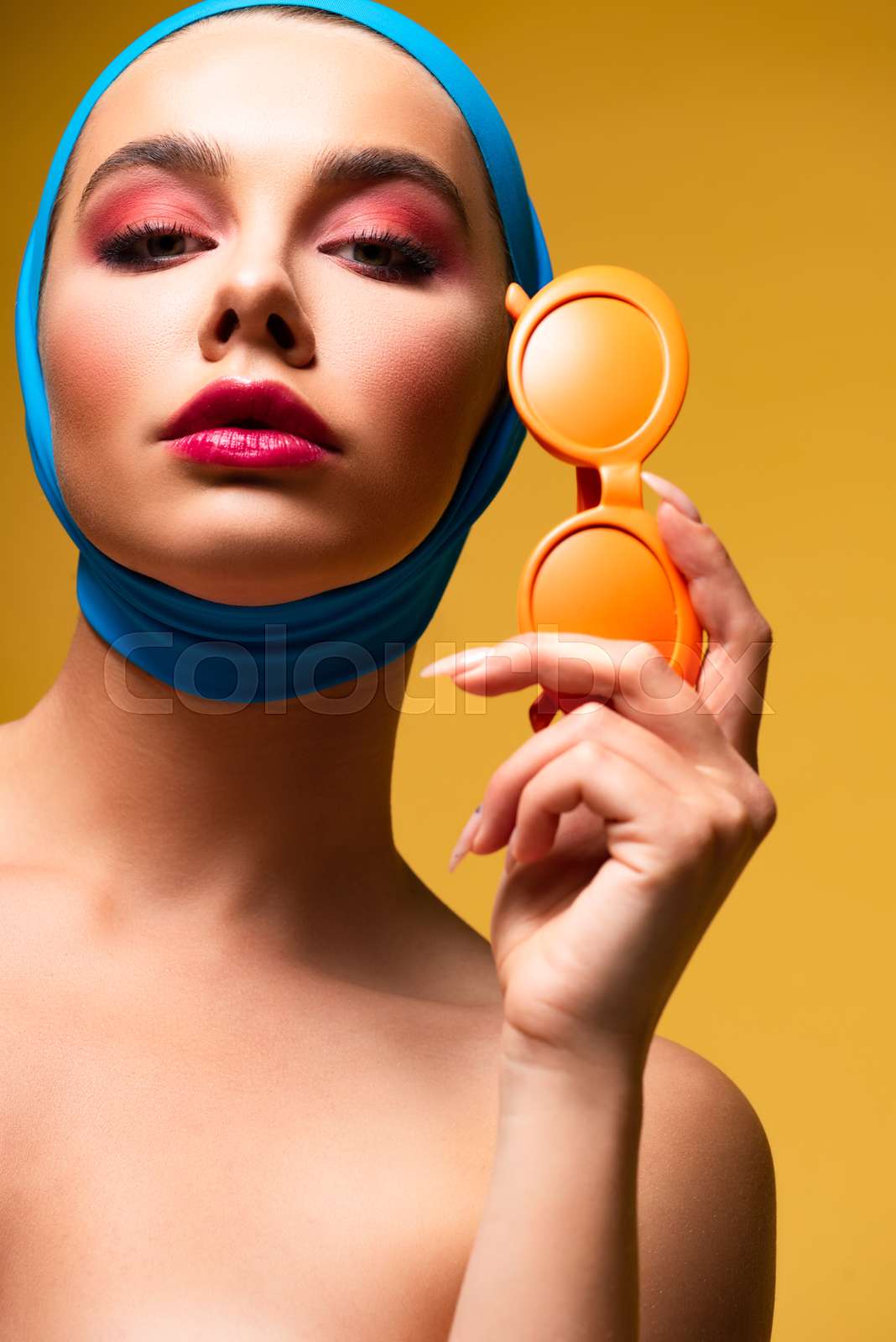 beautiful nude woman in scarf holding sunglasses, on yellow Stock