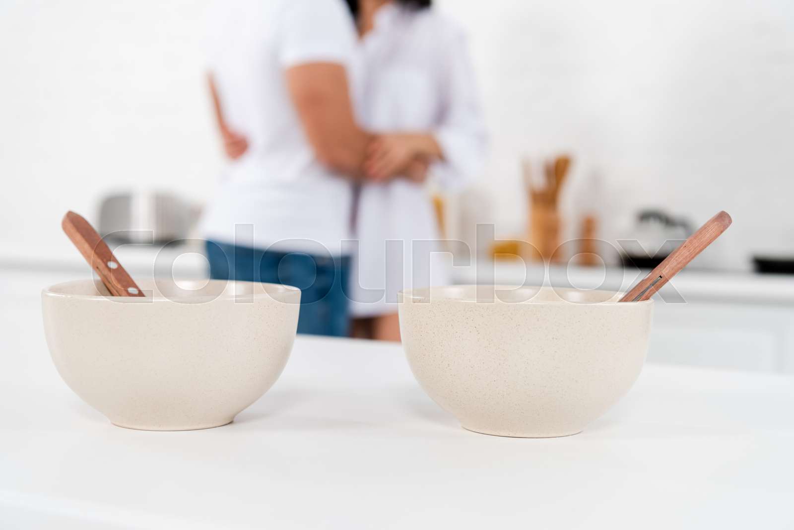Cropped view of couple hugging near bowls with spoons on table in ...