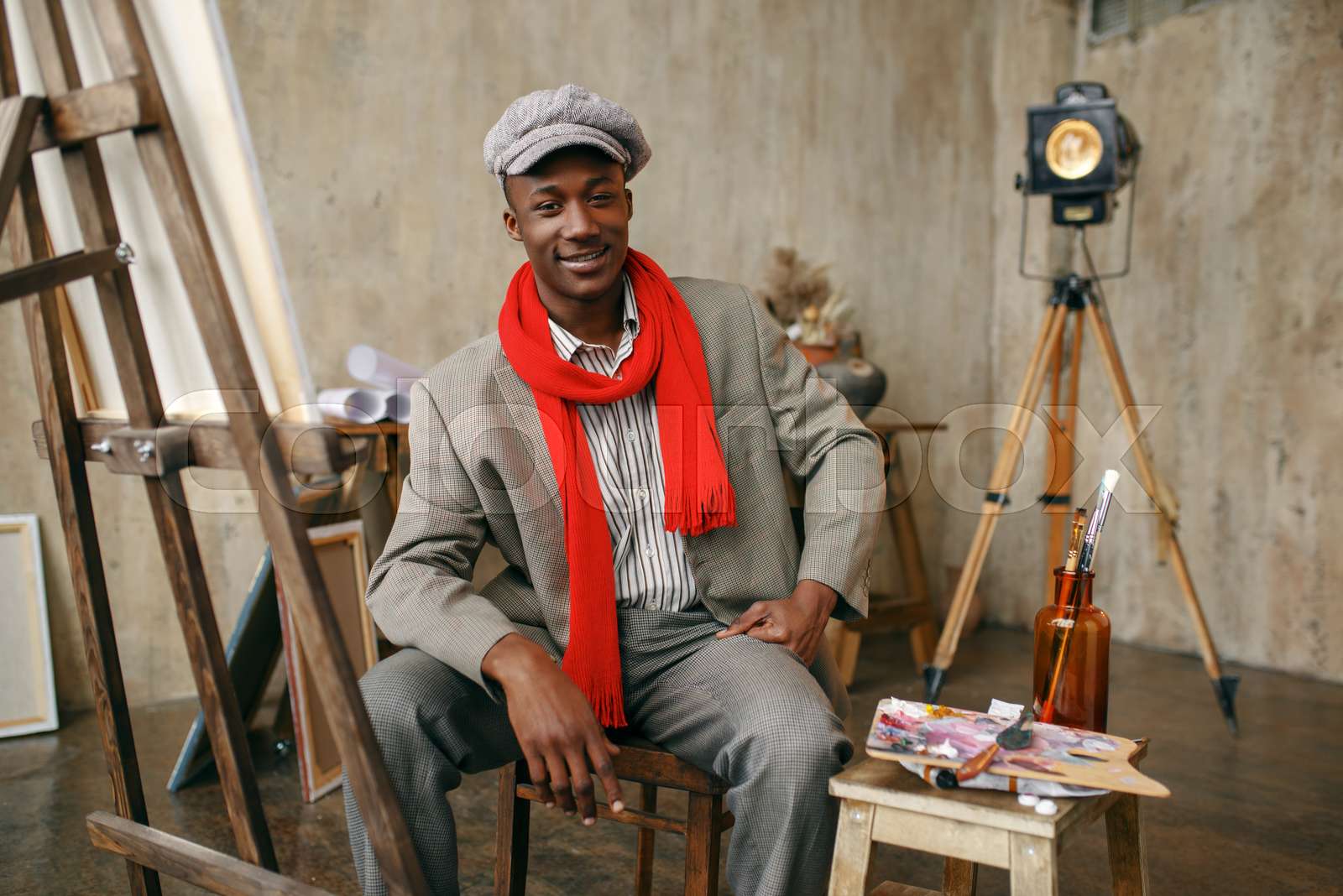 Painter in hat and red scarf poses at easel Stock image Colourbox
