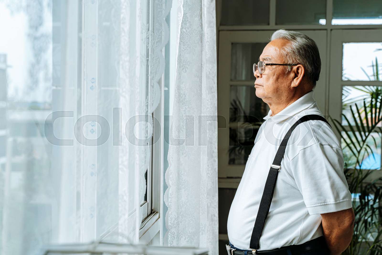 Close up of pensive old man with glasses looking out of window feeling