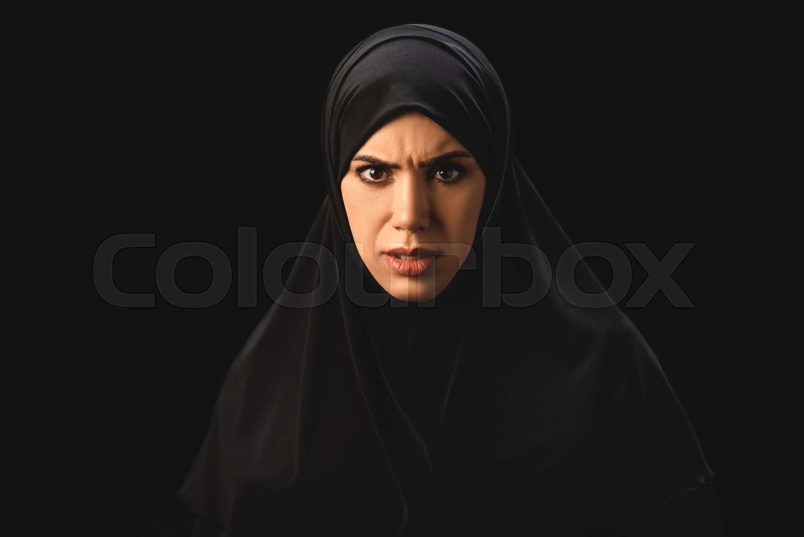 Angry muslim woman in hijab looking at camera isolated on black stock