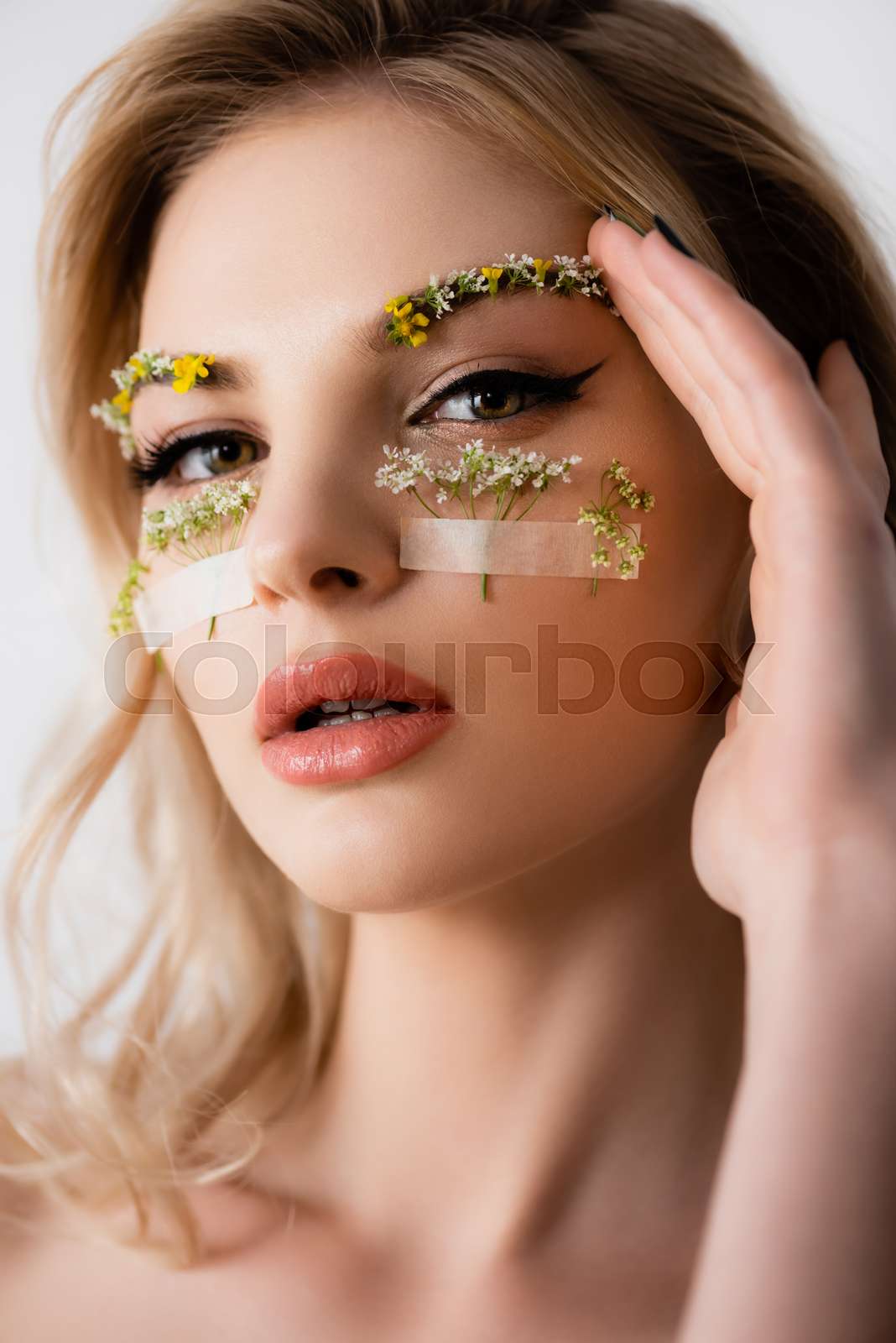 naked beautiful blonde woman with wildflowers under eyes and hand near