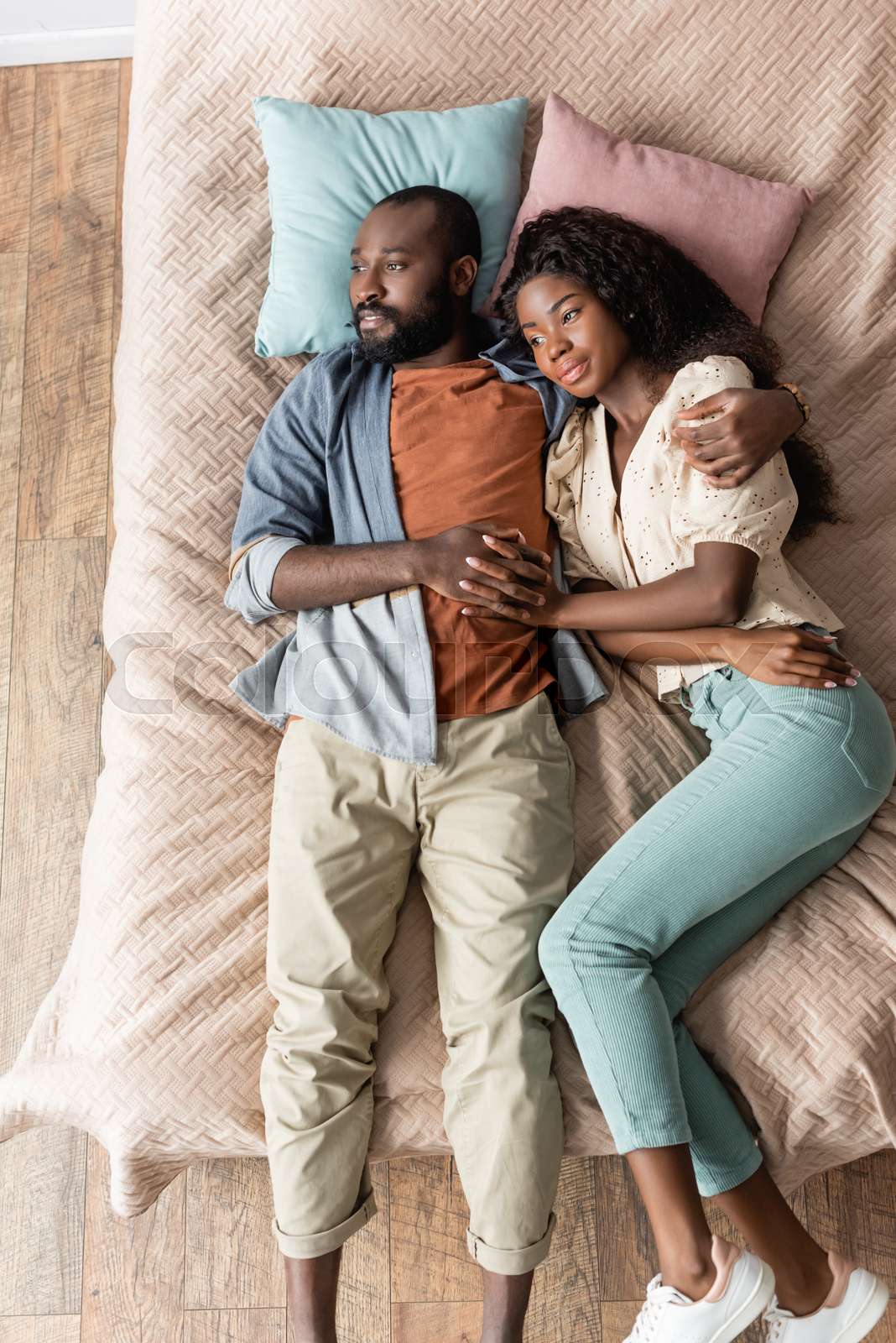 top view of dreamy african american couple embracing while lying in bed ...