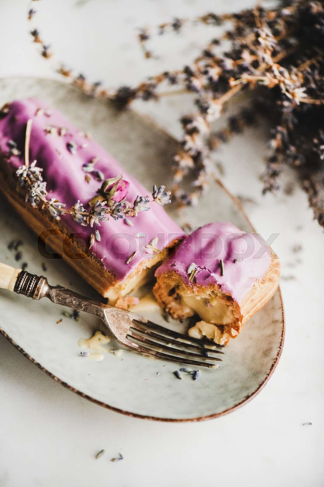 Lavender eclair decorated with purple flowers and branches and fork