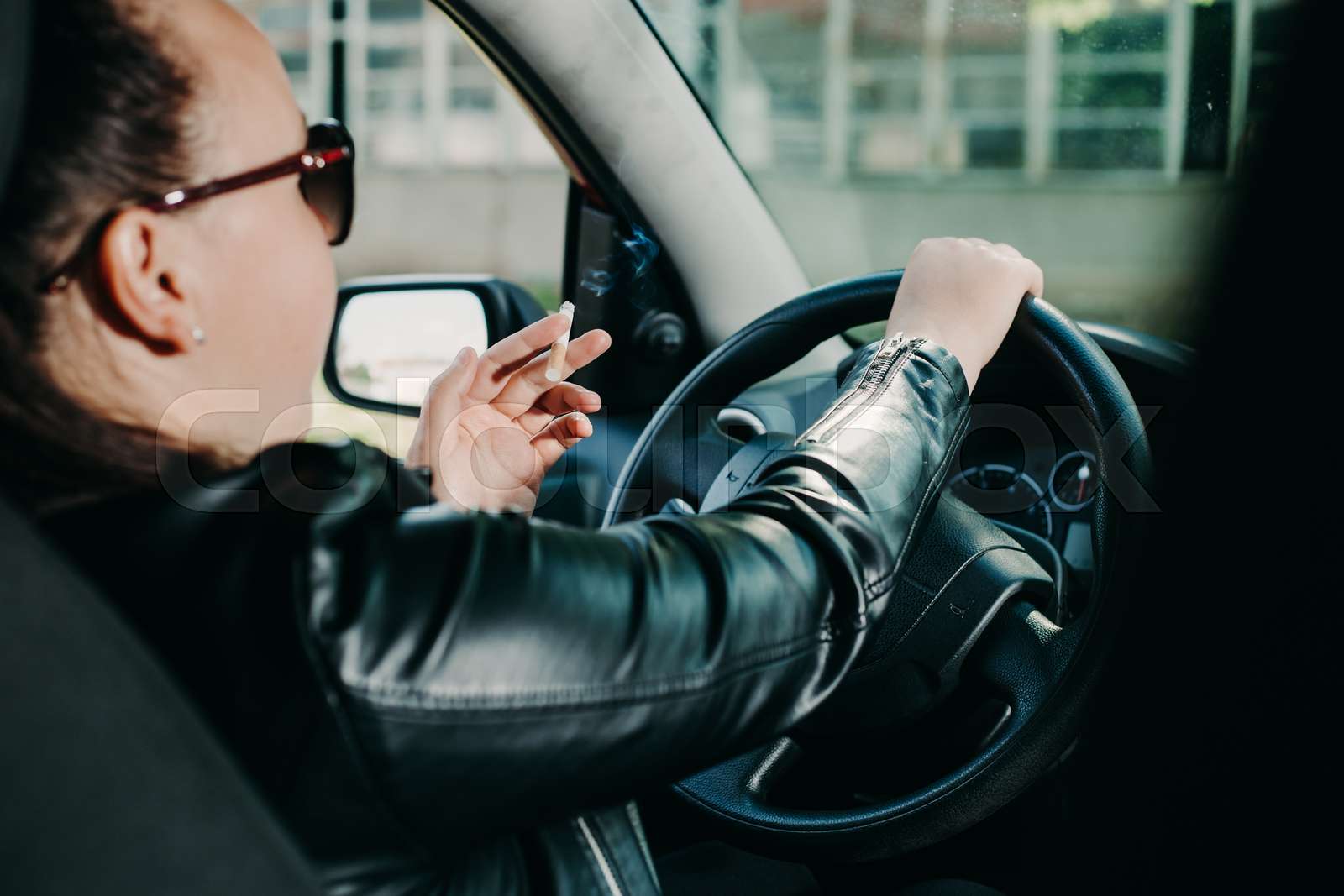 Young woman smoking a cigarette while driving a car, transportation