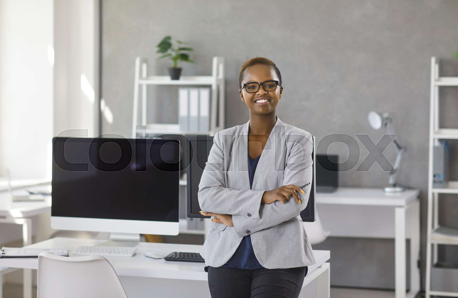Portrait of happy young African American businesswoman standing by desk ...