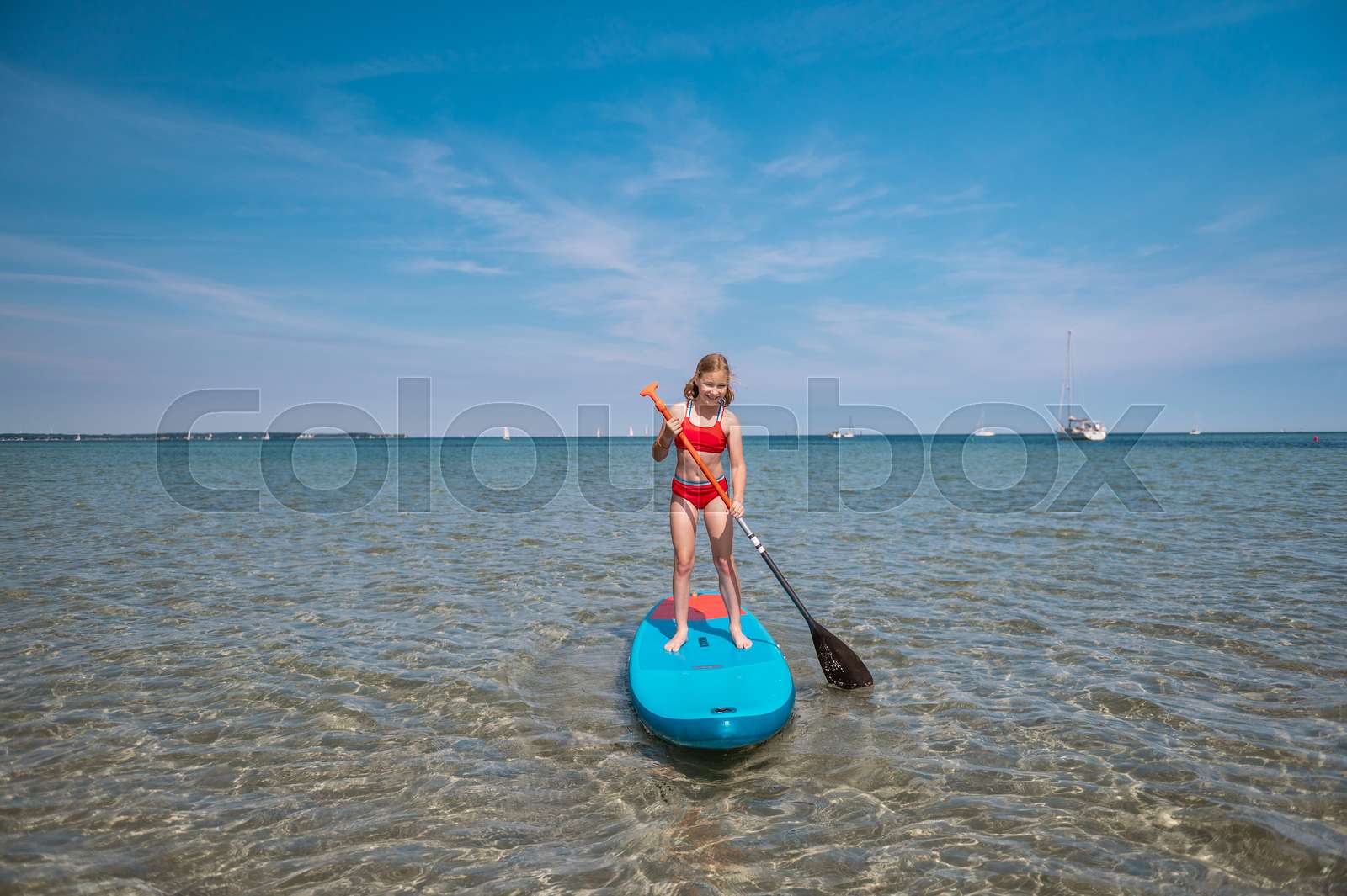 Beautiful teenage girl standing up on paddle board on blue sea at ...