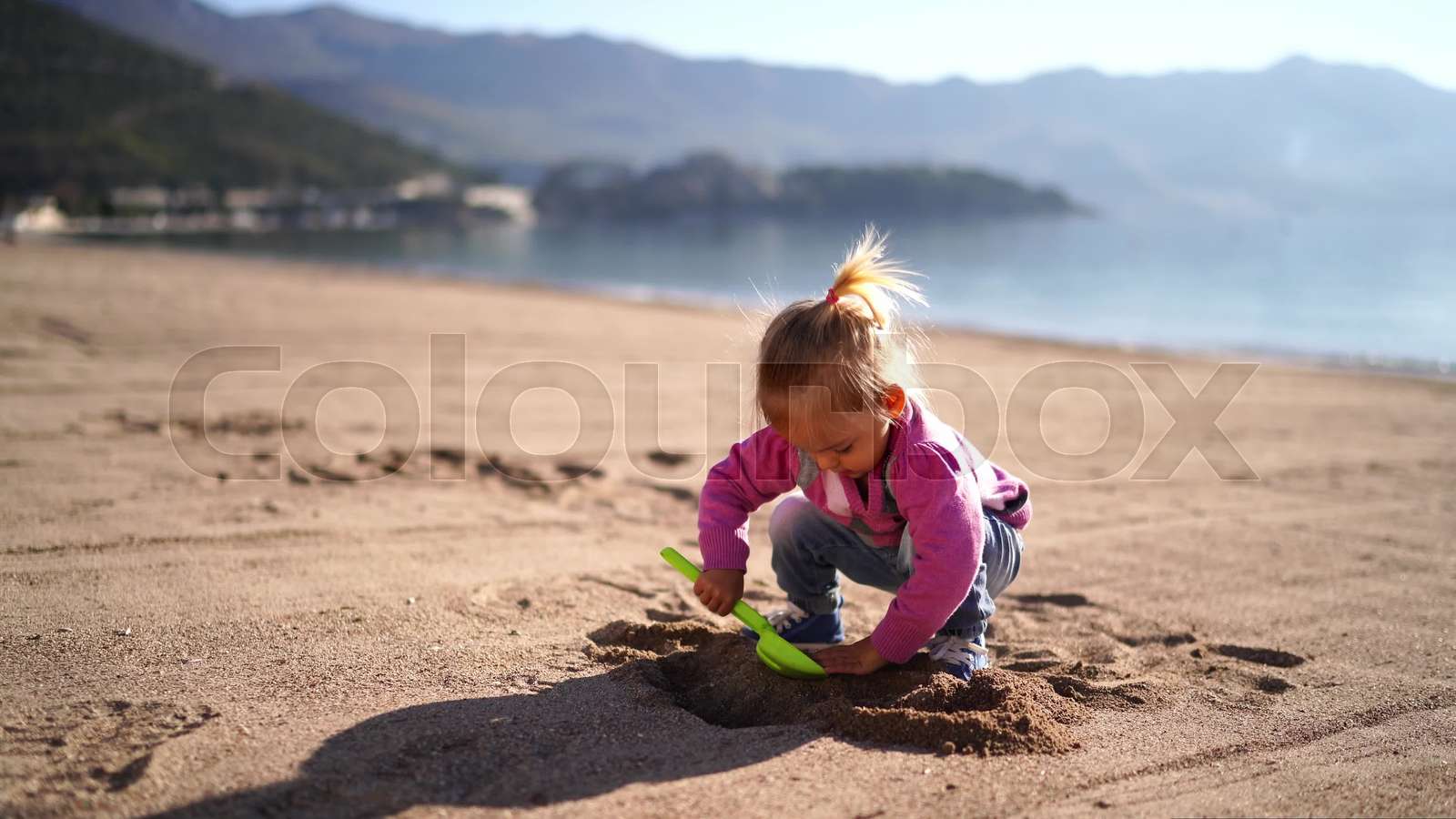 Little girl digs a hole in the sand on the beach with a toy shovel
