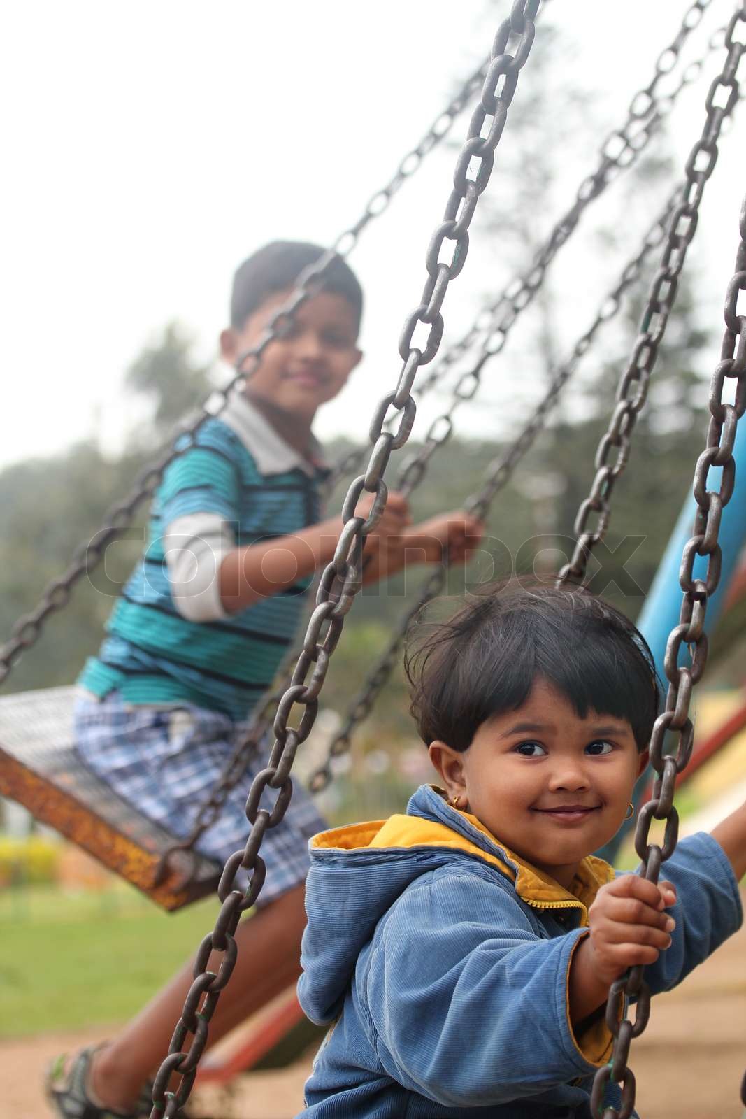 Cute young happy kids playing on swing sets in a park | Stock image ...
