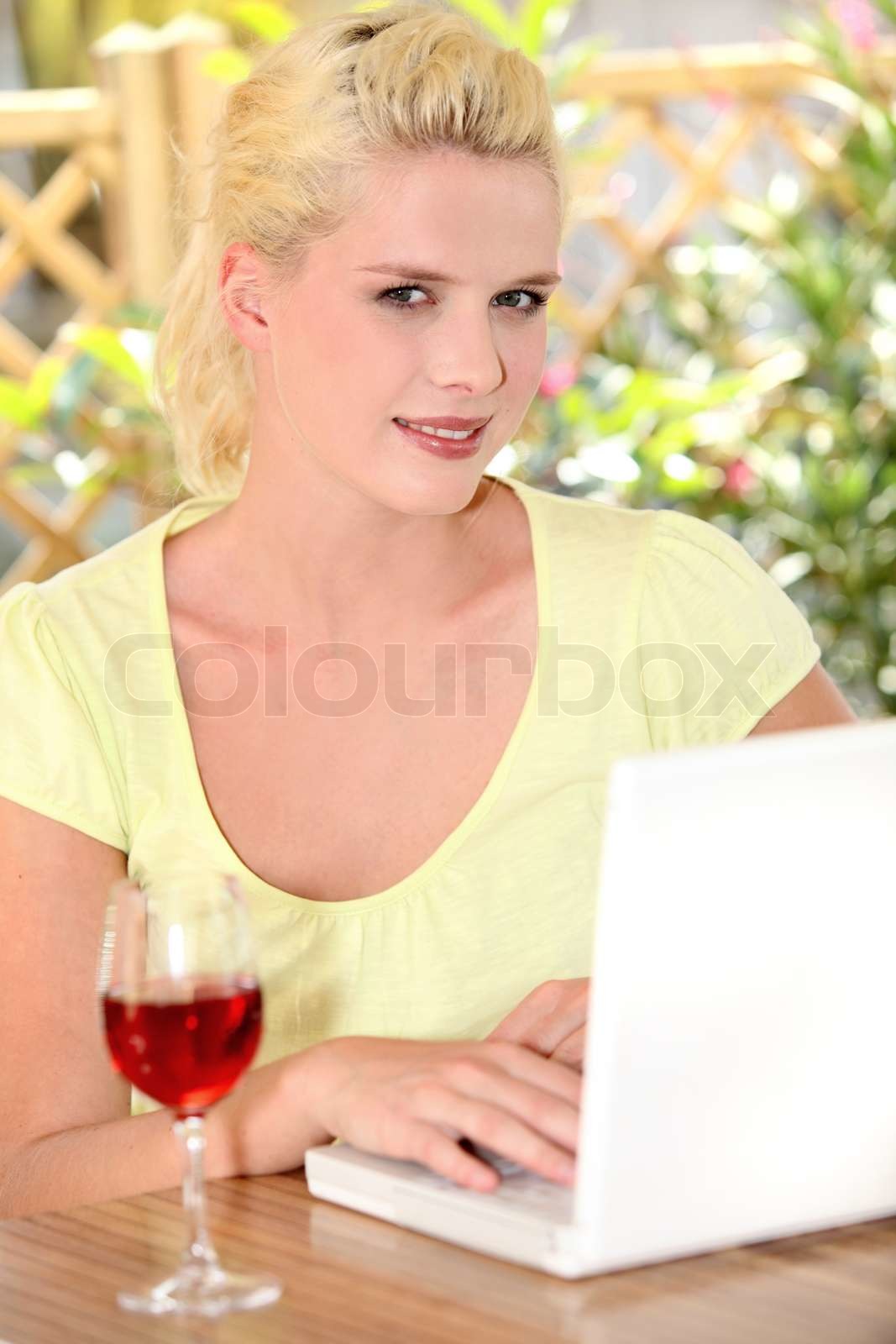 30 Jahre alt blonde Frau, die Computer auf einer Terrasse , gibt es ein Weinglas auf dem Tisch ...