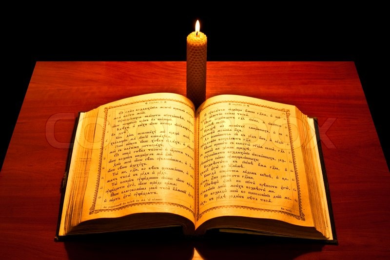 A Bible Open On A Table Next To A Candle A Bible Open On A Table Next To A Candle Stock Photo