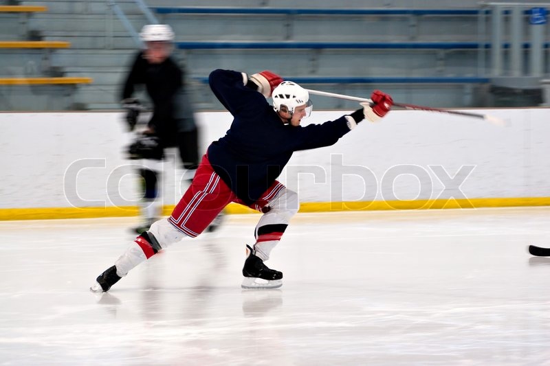 A hockey player shooting the puck as he speeds down the ice. Slight