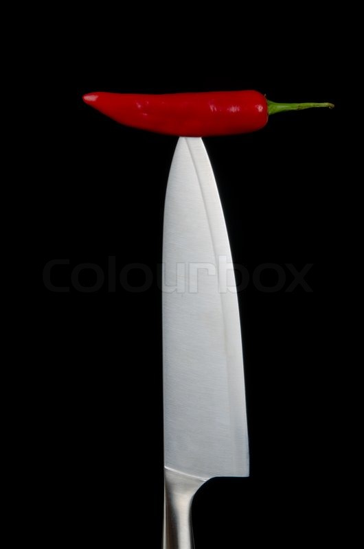 Red chili pepper impaled on a kitchen knife againsta black background