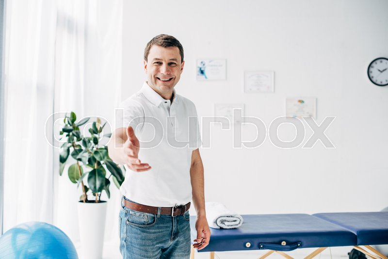 Smiling Chiropractor With Outstretched Hand Looking At Camera In Massage Cabinet Stock Images Page Everypixel