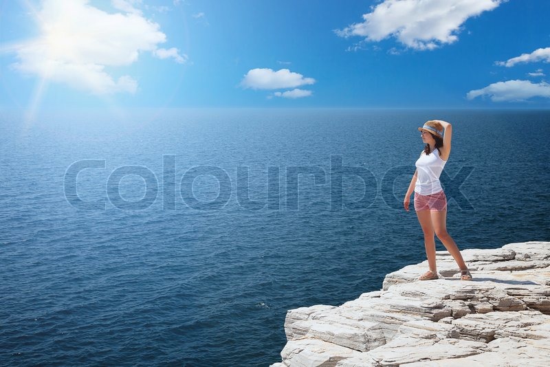 Young Woman Standing On Cliffs Edge And Looking To A Sea Young Woman Standing On Cliffs Edge And Looking To A Sea