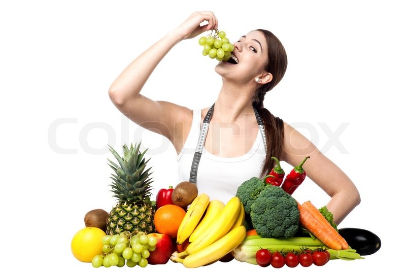 Pretty young girl eating grapes. Fruits and vegetables all around her